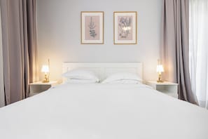 A neatly made bed with white linens, two bedside tables with lamps, and two framed botanical prints on the wall. - Lumiere 3BD with Sea View City Center (Thessaloniki)