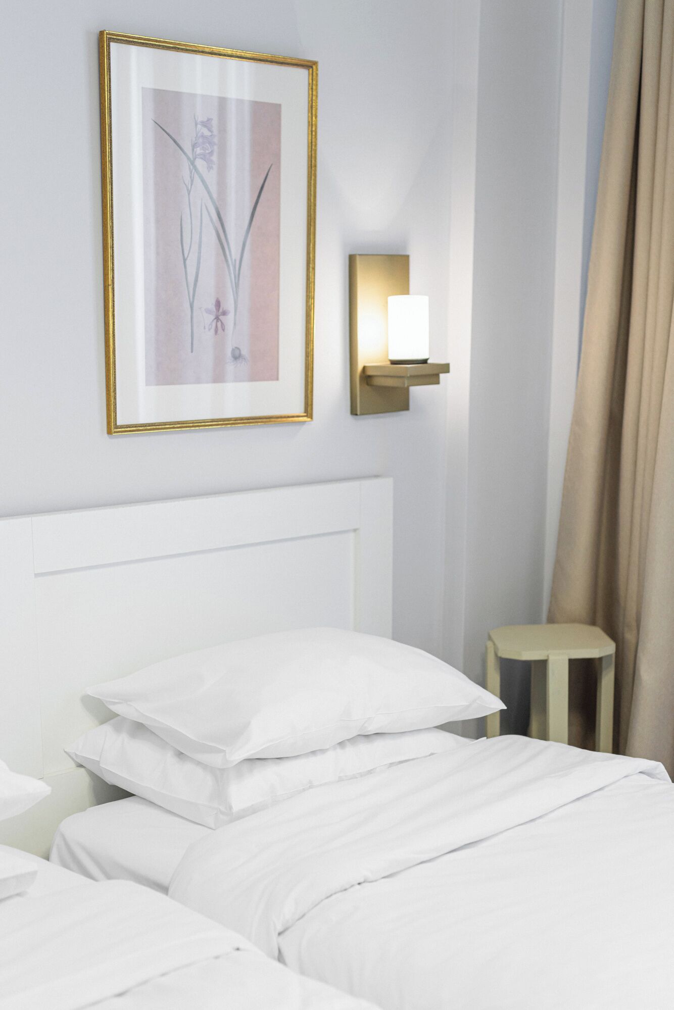 Habitación de hotel con una cama blanca, una obra de arte enmarcada en la pared, una mesita de noche con una lámpara y un pequeño taburete.