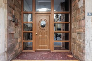 Una puerta doble de madera con un ventanal circular, flanqueada por paneles de vidrio y un cartel con el número 8 en la pared.