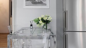 A modern kitchen with a stainless steel refrigerator, a glass dining table with chairs, a framed black and white photo on the wall, and a vase with flowers on the table. - Lumiere 3BD with Sea View City Center (Thessaloniki)