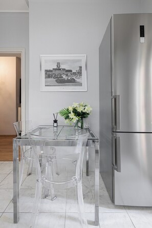 Una cocina moderna con un refrigerador de acero inoxidable, una mesa de comedor de vidrio con sillas, una fotografía en blanco y negro enmarcada en la pared y un florero con flores sobre la mesa.