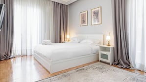 A hotel room with a bed, two bedside tables with lamps, a rug, and curtains. - Lumiere 3BD with Sea View City Center (Thessaloniki)