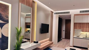 A modern hotel room with a large mirror, a flat-screen TV, a sofa, a dining area, and a kitchen. - Voyage Expo Suites (Riyadh)