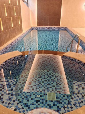 A hot tub with mosaic tile flooring and a tiled wall.