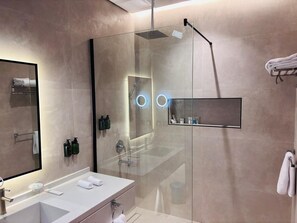 Une salle de bain moderne dotée d’une douche à parois de verre, d’un grand miroir et d’un meuble-lavabo avec un évier et un porte-serviettes.