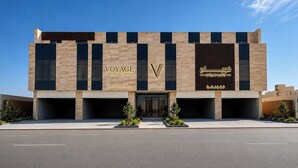 A modern building with 'VOYAGE EXPO SUITES' signage, featuring a prominent 'V' logo, and Arabic script on the right side. - Voyage Expo Suites (Riyadh)