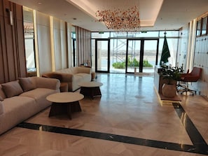 Un hall amplio con un diseño moderno, que cuenta con un sofá grande, dos mesas redondas para café y una zona de estar con una silla roja.