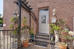 A brick building with a white door, potted plants, and a metal gate.