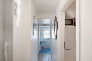 A narrow hallway with a white door at the end, a white wall with a decorative mirror, and a microwave above a white cabinet.