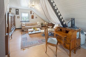 A cozy loft bedroom with a sloped ceiling, a wooden desk, a chair, a sofa, and a dresser.