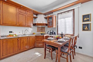A kitchen with wooden cabinets, a dining table with chairs, and a window with a curtain. - Toniol Apartment (Riva del Garda)