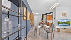 A modern dining area with a glass table, chairs, and a view of the kitchen. - Toniol Apartment (Riva del Garda)