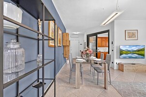 A modern dining area with a glass table, chairs, and a view of the kitchen.