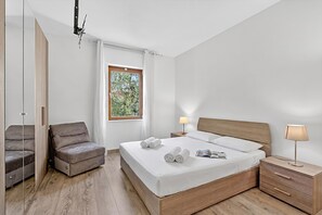 Ein Schlafzimmer mit einem Bett, Nachttischen, einem Sessel und einem Fenster.