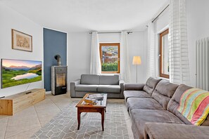 A modern living room with a sofa, a coffee table, a TV, a fireplace, and a window with curtains. - Toniol Apartment (Riva del Garda)