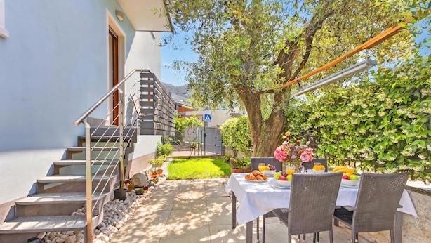 A patio with a table set for dining, a staircase, and a garden area. - Toniol Apartment (Riva del Garda)