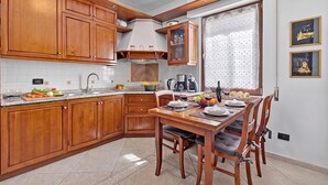 A kitchen with wooden cabinets, a dining table with chairs, and a window with a curtain. - Toniol Apartment (Riva del Garda)