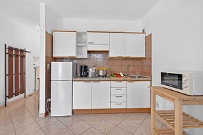 A modern kitchen with white cabinets, a stainless steel refrigerator, a microwave, and a wooden table.