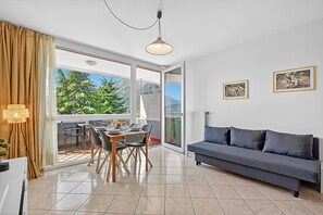 Una sala de estar moderna con sofá, mesa de comedor, sillas y un ventanal con vistas a zonas verdes.