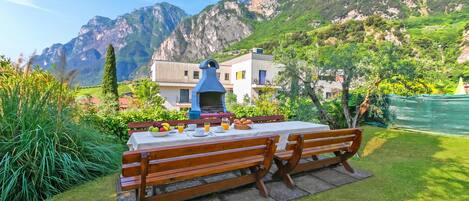 Una mesa para comer con bancos, una chimenea azul y montañas al fondo.