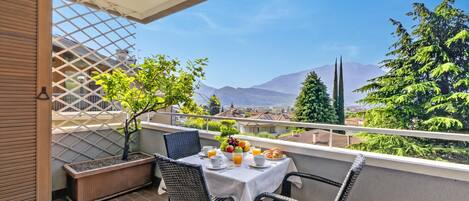 A balcony with a table set for breakfast, a potted plant, and a view of mountains.