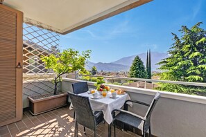 A balcony with a table set for breakfast, a potted plant, and a view of mountains.