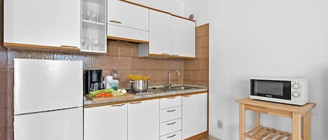 A kitchen with white cabinets, a microwave on a wooden cart, and a sink.