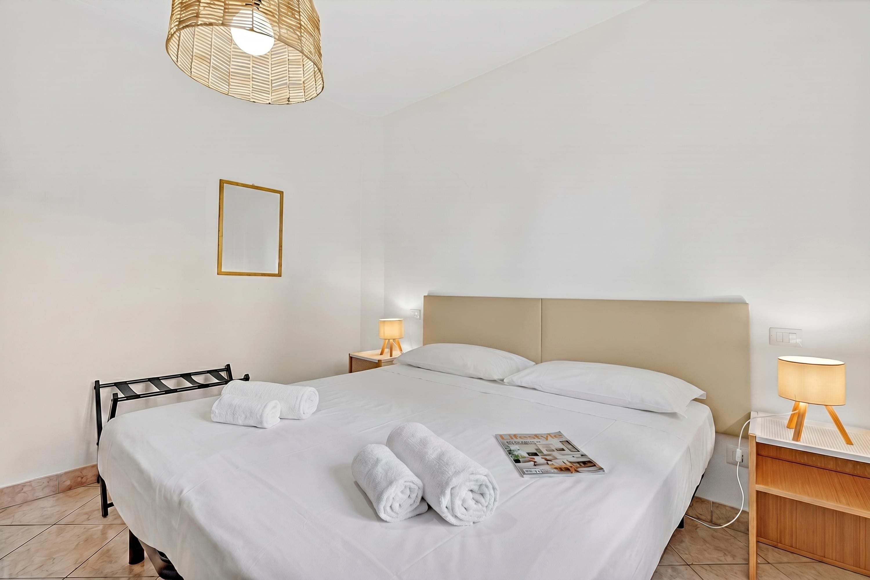 Een hotelkamer met een bed, twee nachtkastjes, een lamp, een tijdschrift en een stoel.