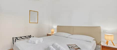 A hotel room with a bed, two bedside tables, a lamp, a magazine, and a chair.