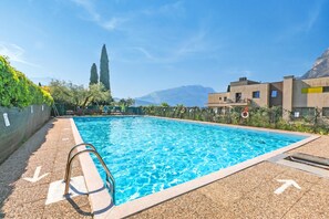 A swimming pool with a metal ladder, clear blue water, and a view of mountains in the background. - Lagotissimo 17 - Flat With Balcony View and Pool (Riva del Garda)
