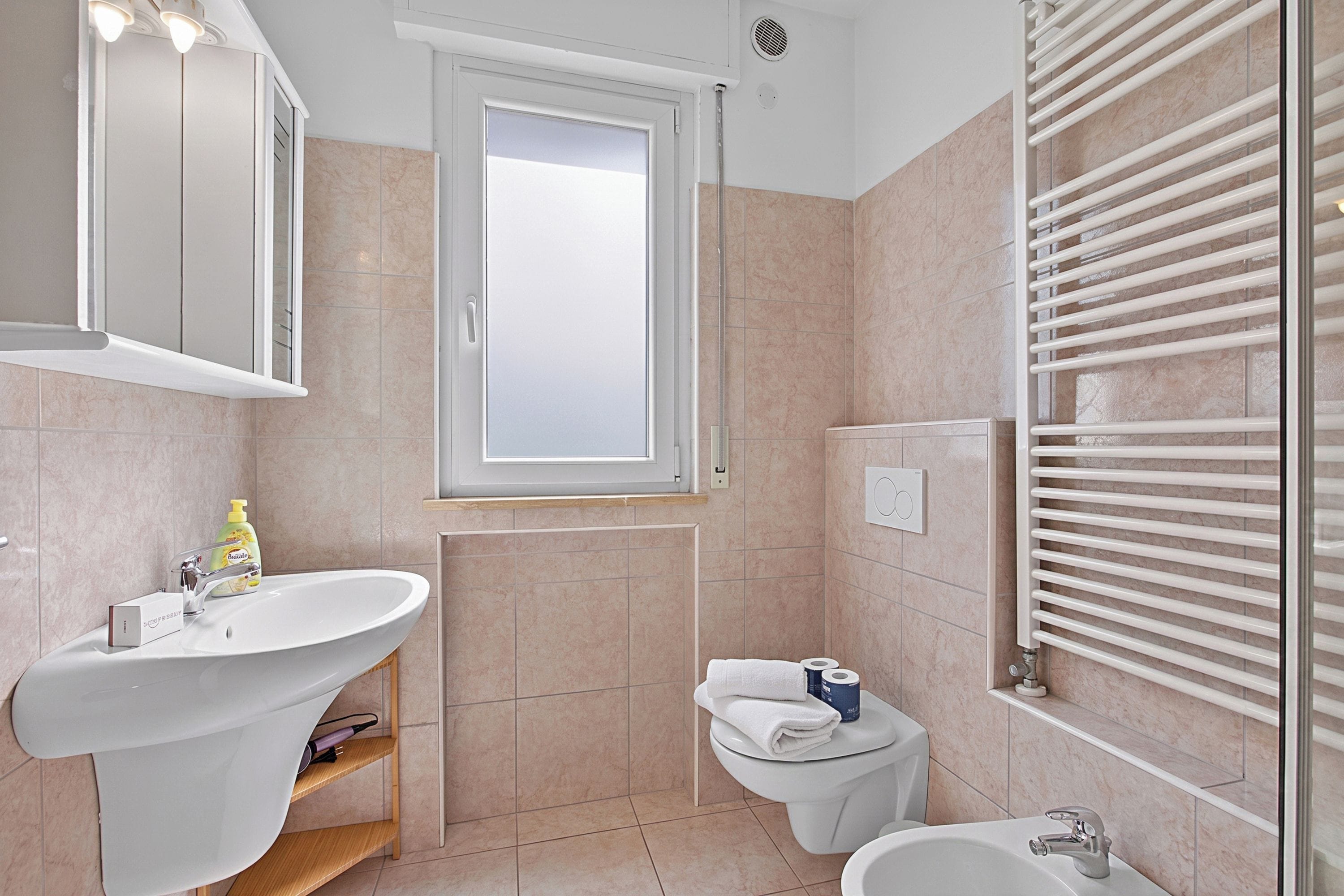 A bathroom with a sink, toilet, bidet, and a window.