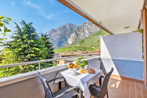 A balcony with a table set for breakfast, wicker chairs, and a mountain view. - Lagotissimo 17 (Riva del Garda)