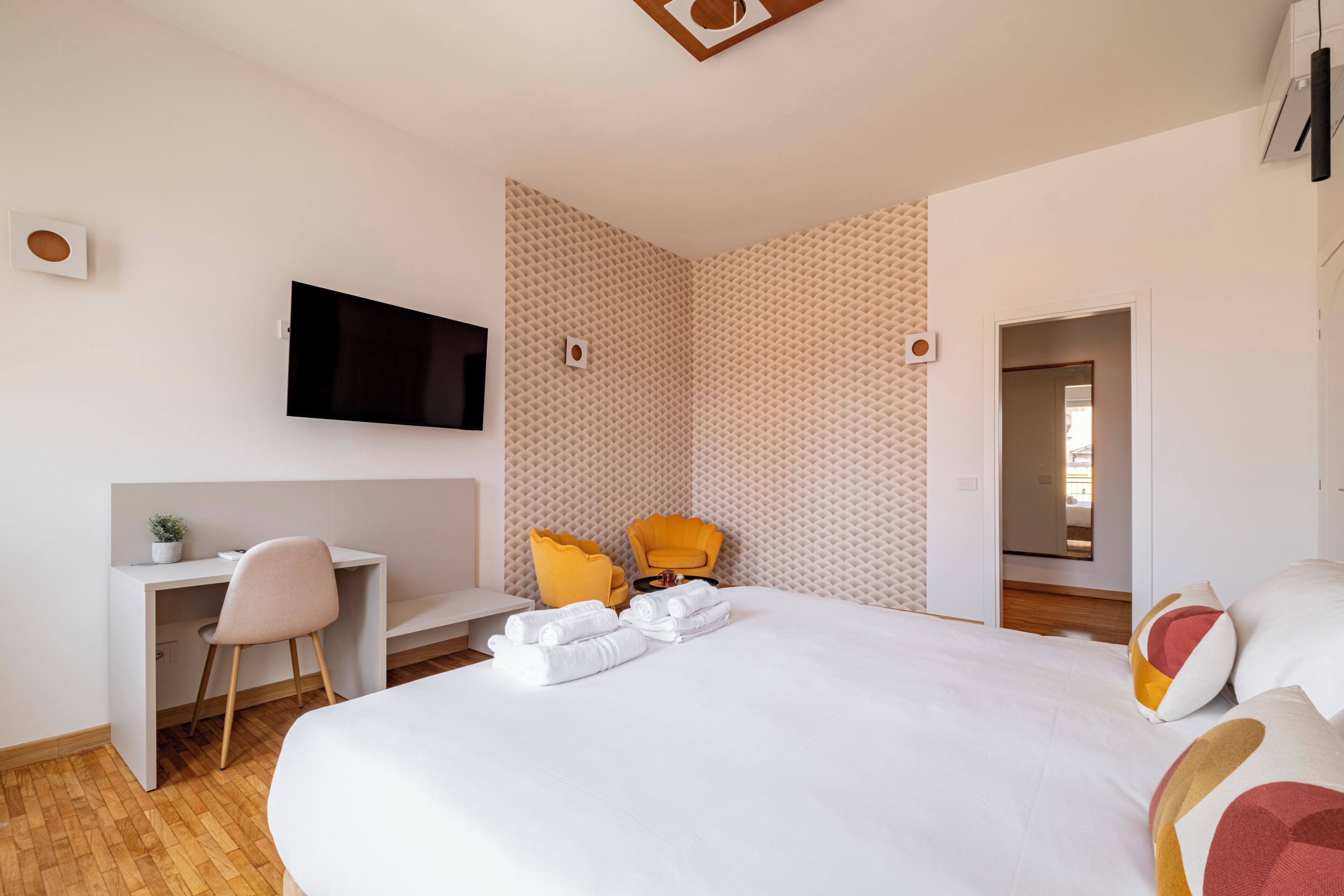 Ein modernes Hotelzimmer mit einem Bett, einem Schreibtisch, einem Sessel und einem an der Wand befestigten Fernseher.