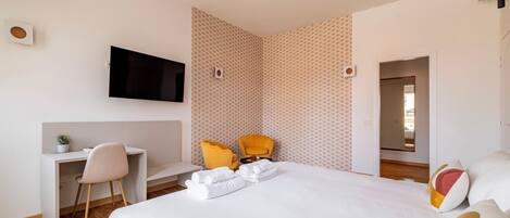 Ein modernes Hotelzimmer mit einem Bett, einem Schreibtisch, einem Sessel und einem an der Wand befestigten Fernseher.