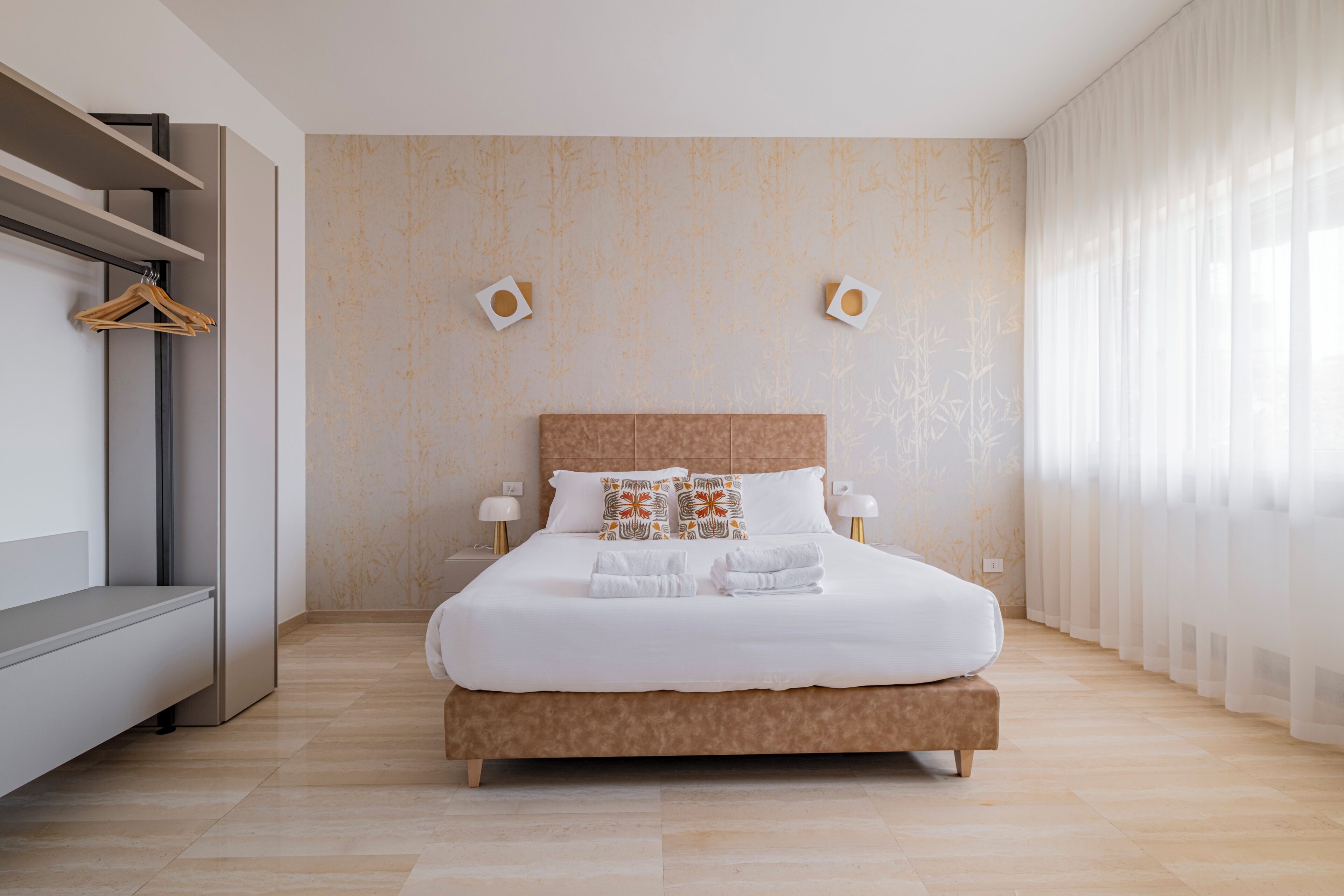 A modern hotel room with a large bed, bedside tables, a wardrobe, and a view of the outdoors.