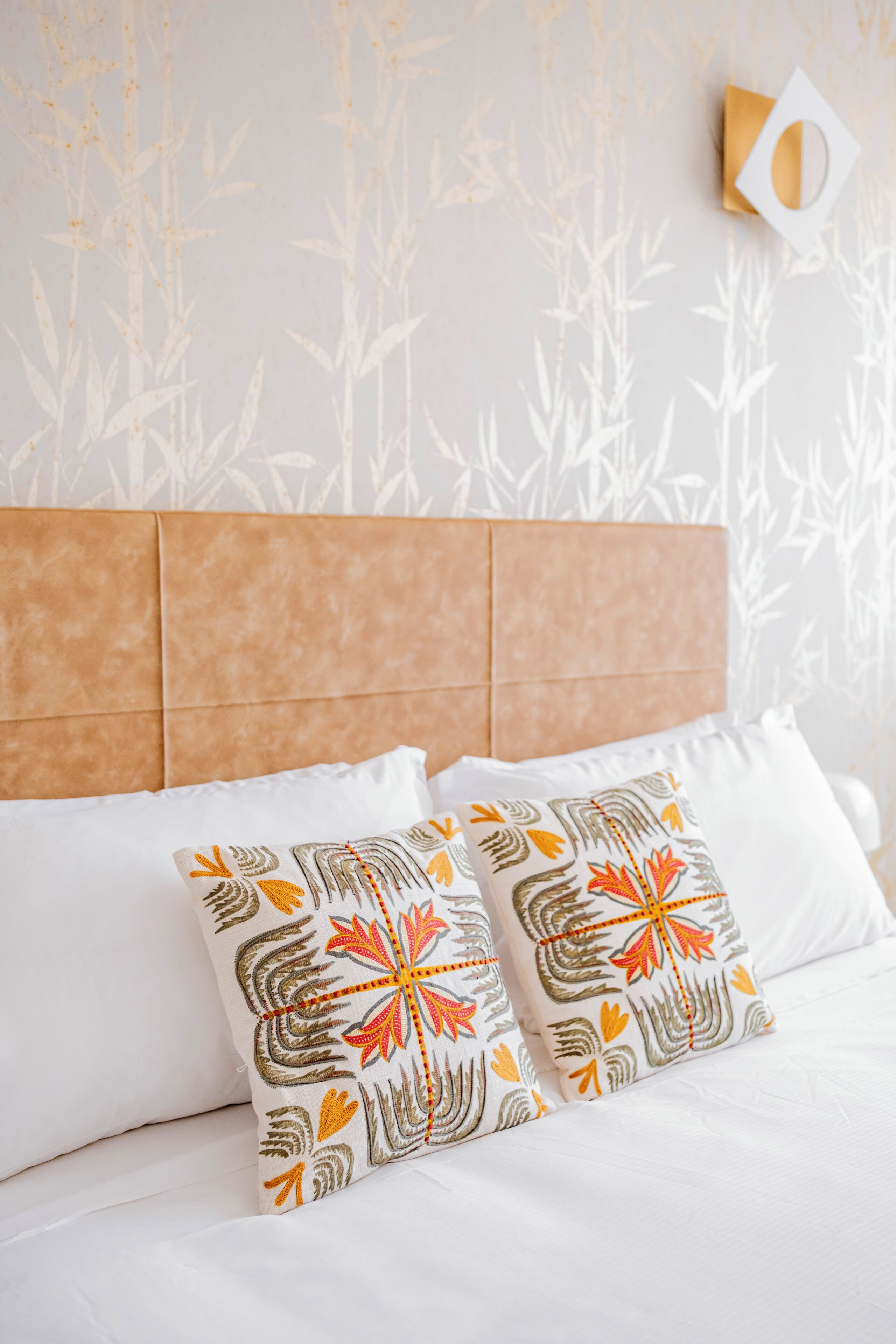 A bed with white bedding and decorative pillows, a headboard, and a wall with a subtle pattern.