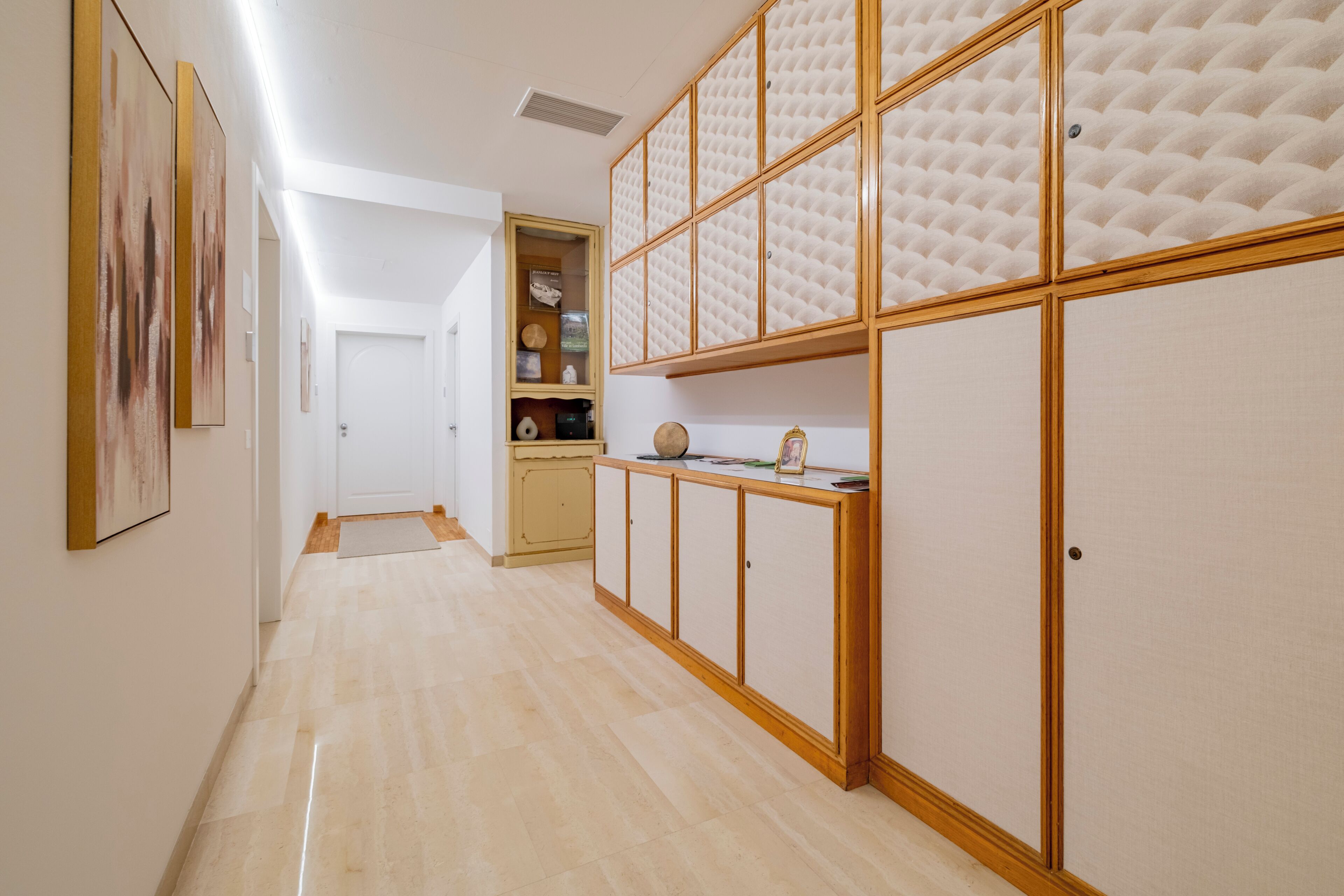 A hallway with a wooden cabinet, a door, and a shelf with items.