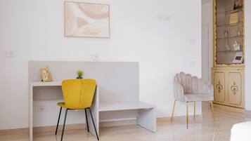 A modern room with a white desk, a yellow chair, a grey armchair, and a cabinet with glass doors.