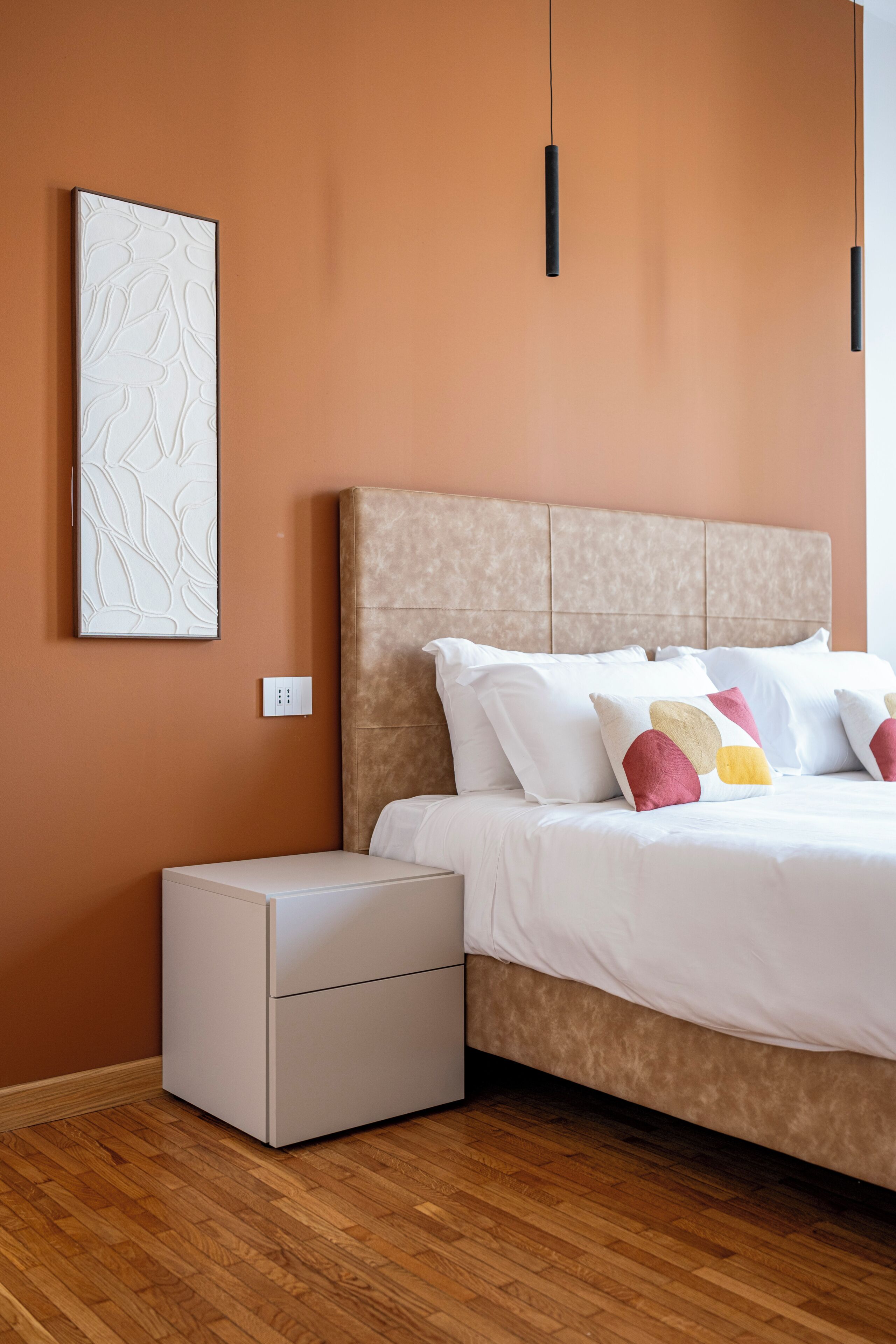Ein Schlafzimmer mit Bett, Nachttisch, Wandbild und Pendelleuchten.