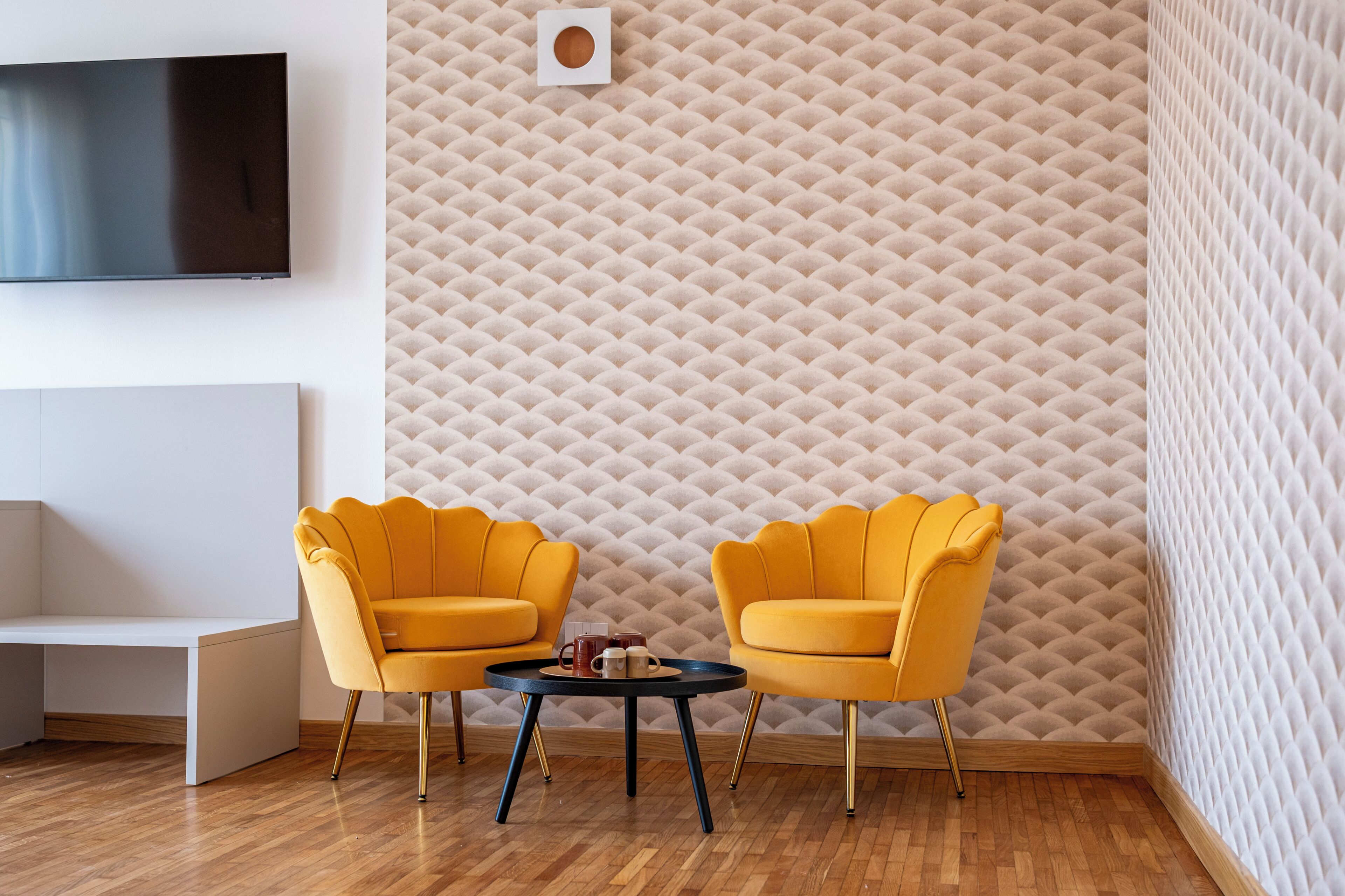 A modern living room with a flat-screen TV, two yellow armchairs, a small round table, and a textured wall.