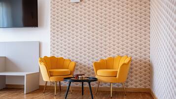 A modern living room with a flat-screen TV, two yellow armchairs, a small round table, and a textured wall.