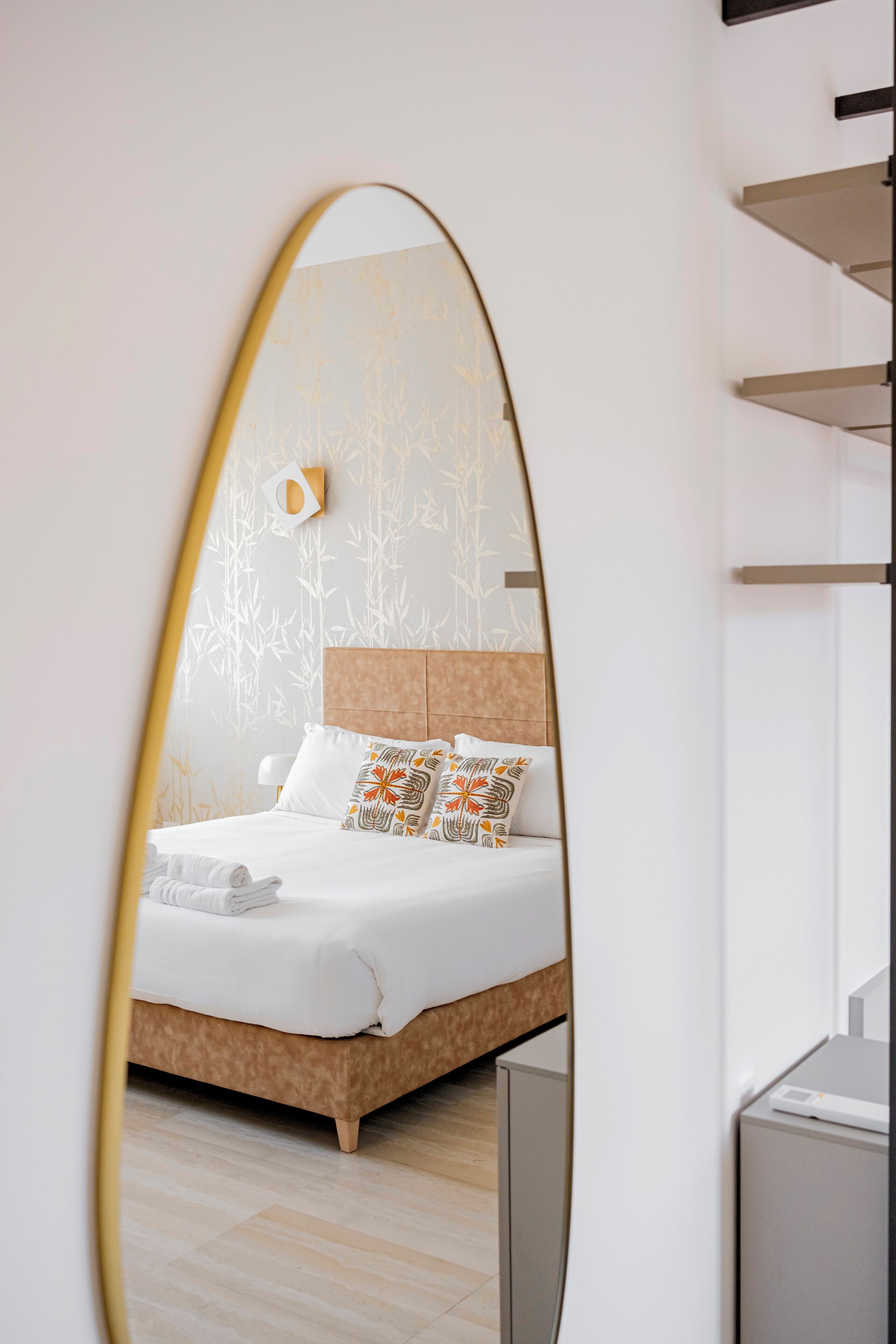 A modern hotel room with a large bed, a mirror, and a wall with a bamboo pattern.