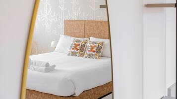 A modern hotel room with a large bed, a mirror, and a wall with a bamboo pattern.