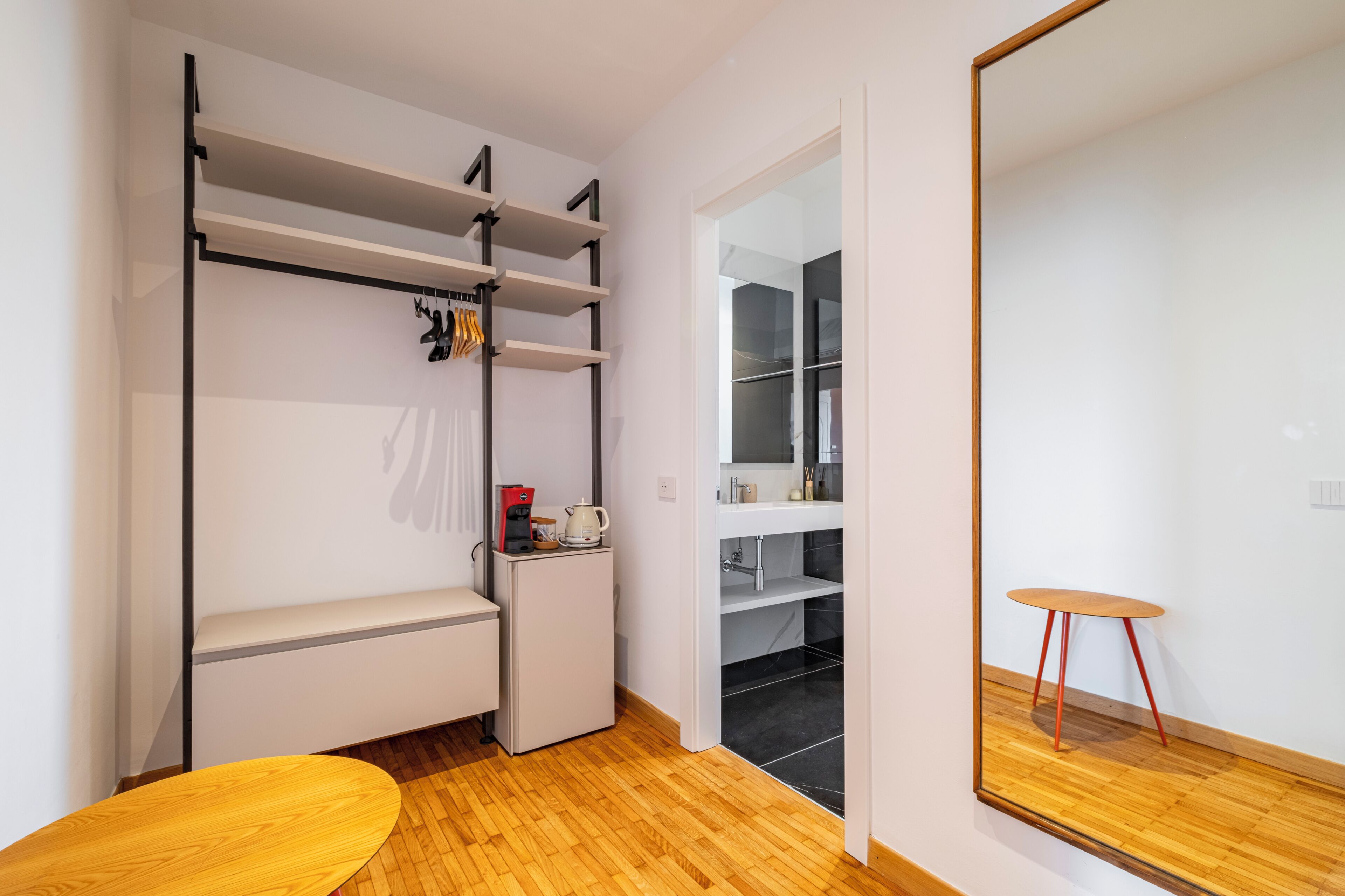 A compact room with a kitchenette, a small seating area, and a mirror reflecting the room.