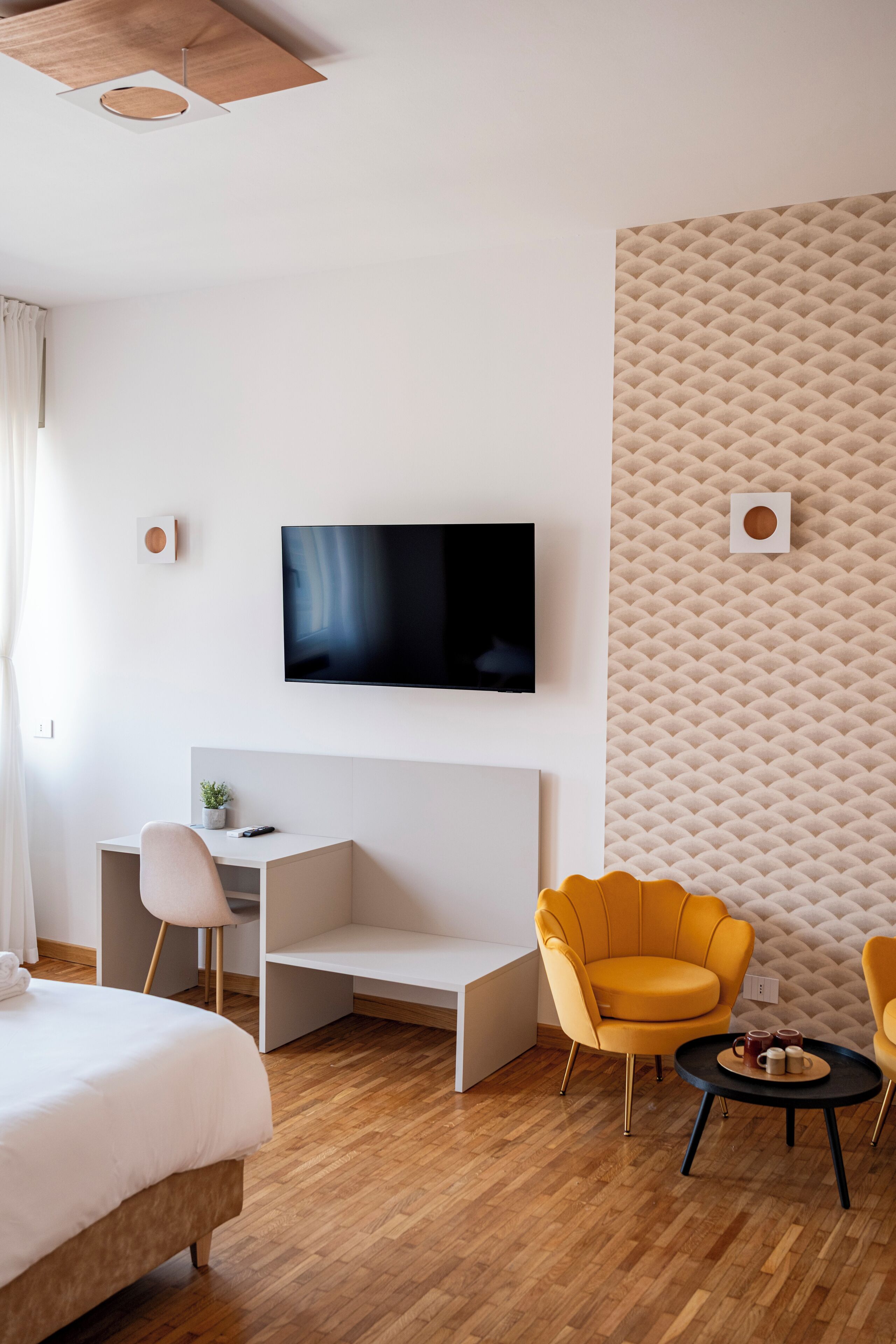 Ett modernt hotellrum med en säng, ett skrivbord, en tv och två gula stolar.