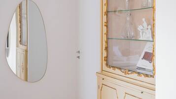 Una habitación con un espejo grande en la pared, un aparador de vidrio con objetos decorativos y suelo de madera.