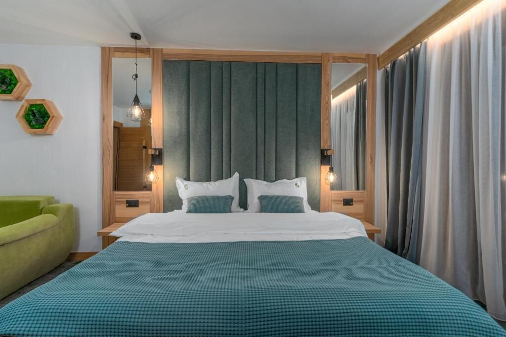 A hotel room with a bed, green curtains, a green sofa, and a wooden headboard.