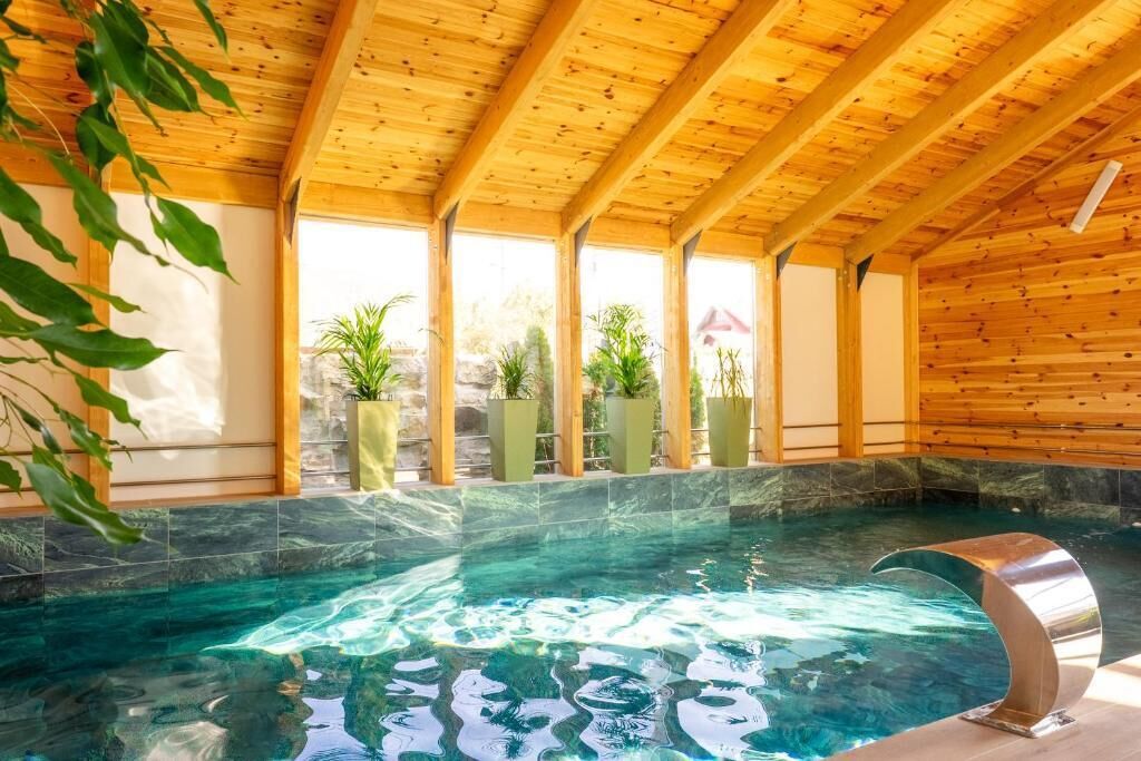 An indoor swimming pool with wooden beams, clear water, and potted plants.
