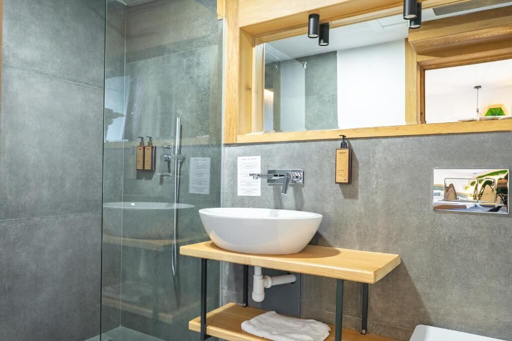 A modern bathroom with a glass shower enclosure, a white vessel sink, and a wooden vanity.