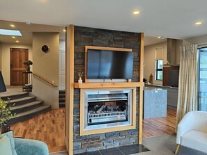Ein modernes Wohnzimmer mit Kamin, Fernseher und einer Küche im Hintergrund.